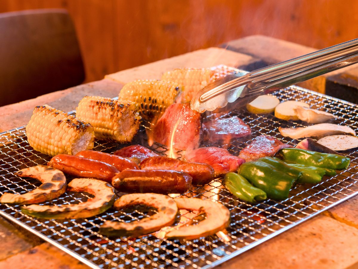 Meat, corn, and vegetables cooking over charcoal grill